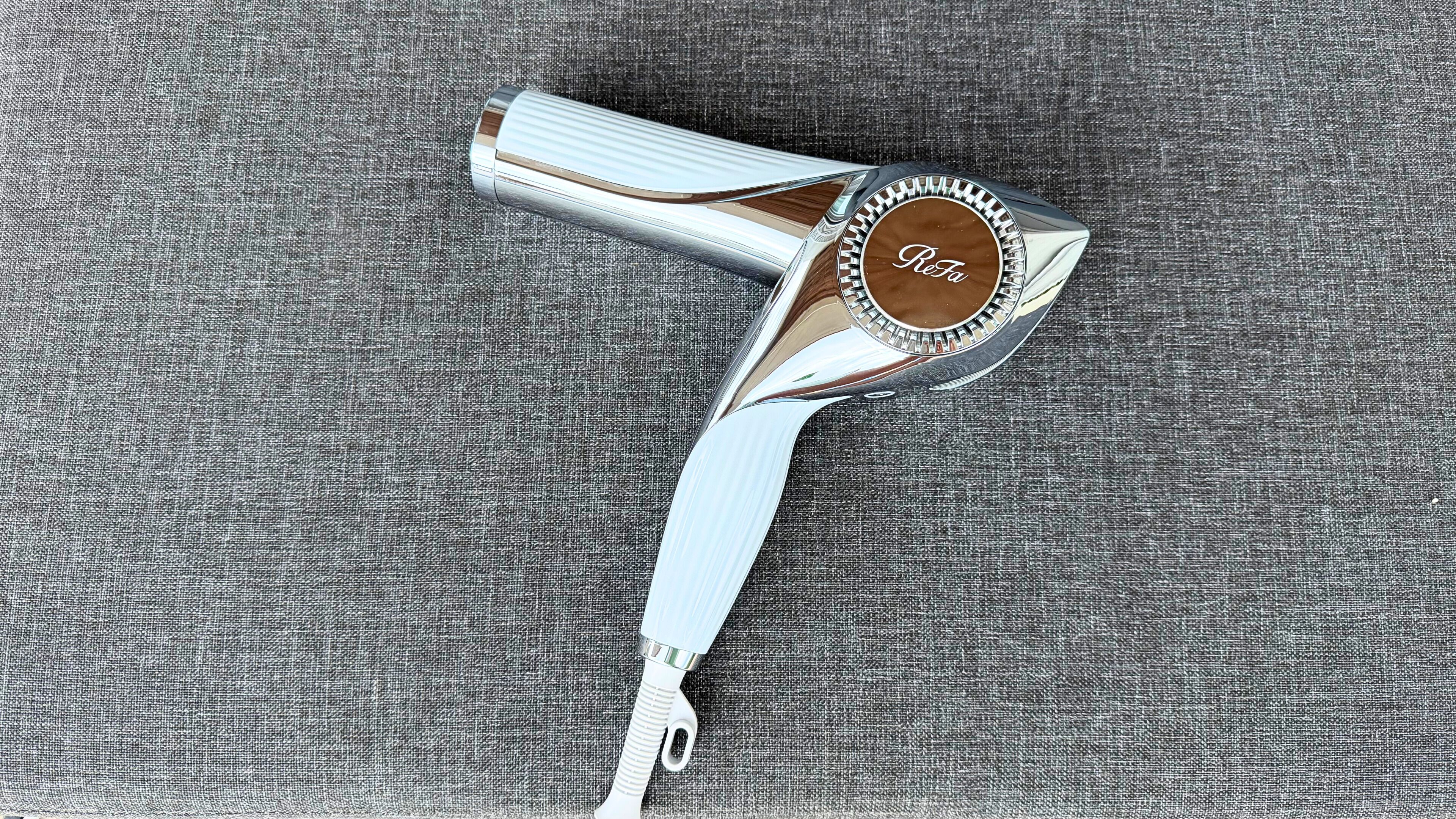 Een metalen haardroger met handvat en een rond voetstuk op een stoffen oppervlak met structuur.