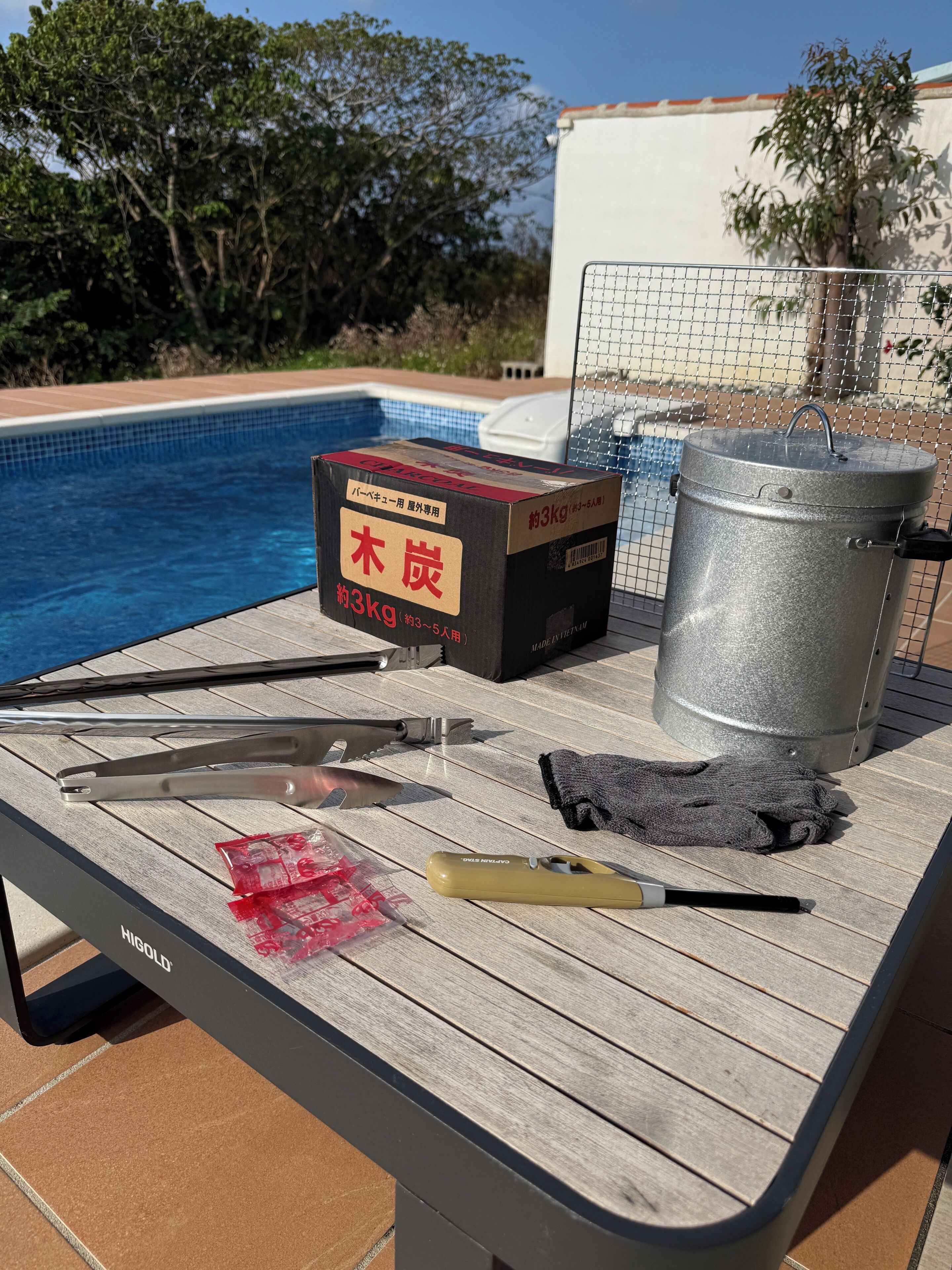 A poolside table with a metal pot, a box, and various tools.