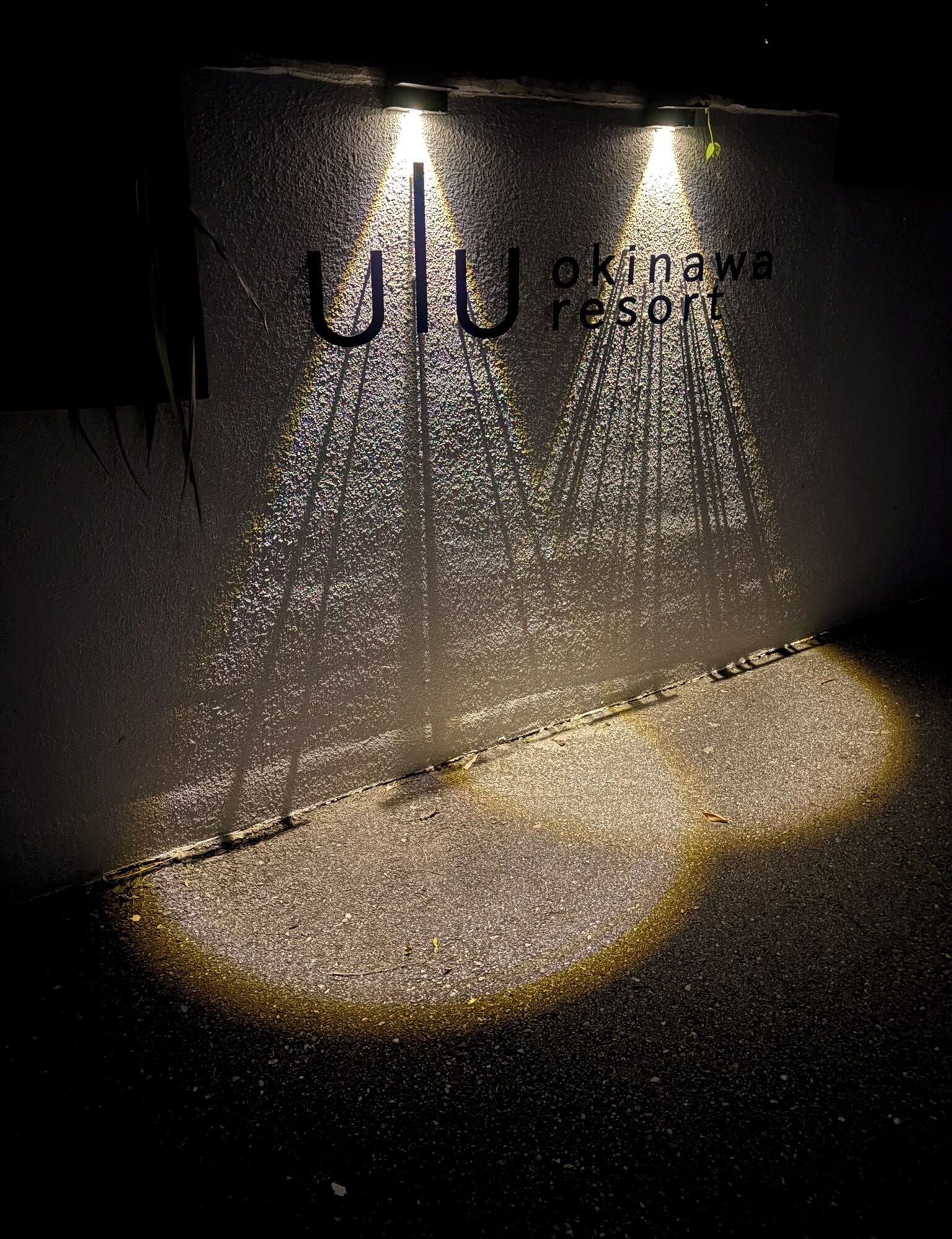 A sign for Ulu Okinawa Resort with a reflection of a bridge structure.