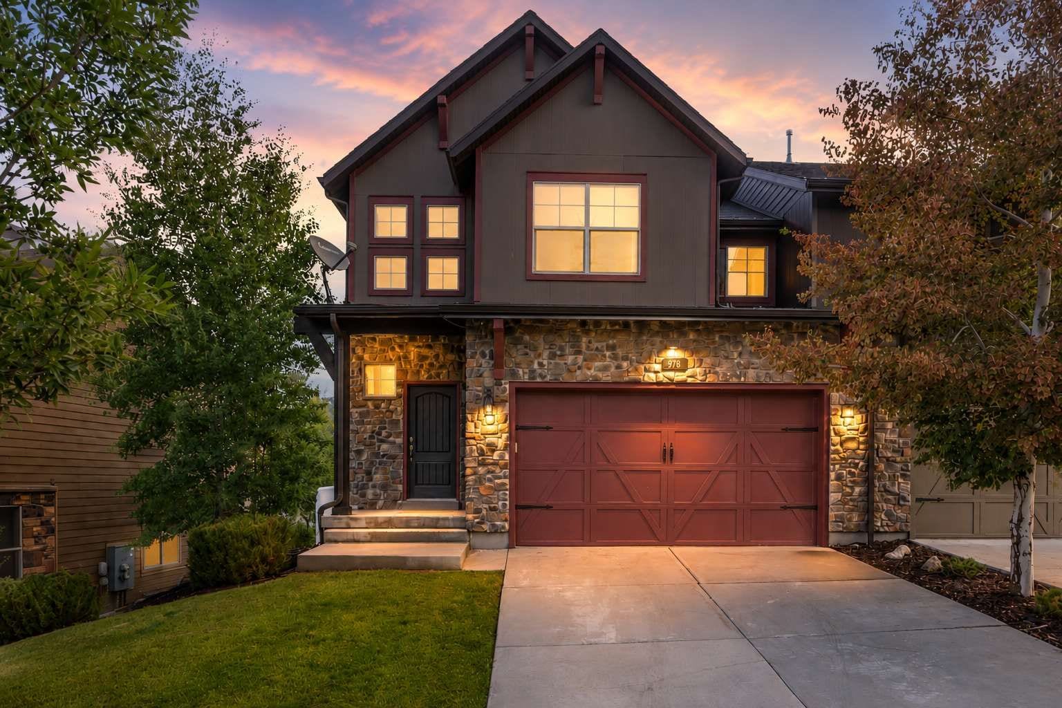 A two-story house with a stone facade, a red garage door, and a well-maintained lawn.