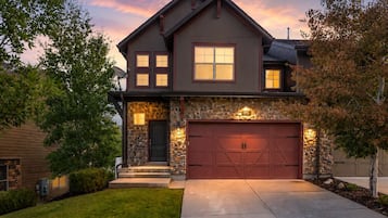 A two-story house with a stone facade, a red garage door, and a well-maintained lawn.