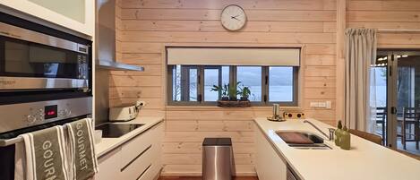 A modern kitchen with wooden walls, a stainless steel oven, a clock, and a view of the outdoors.