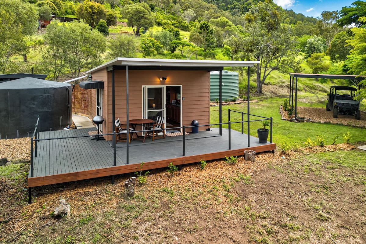 A small cabin with a deck, a barbecue area, and a view of the surrounding forest.