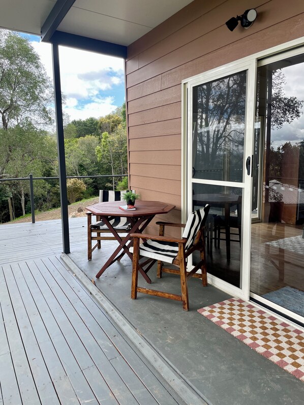 A covered patio with a wooden table and chairs, a sliding glass door, and a view of the surrounding greenery. - The Archer Retreat (Mount Archer)