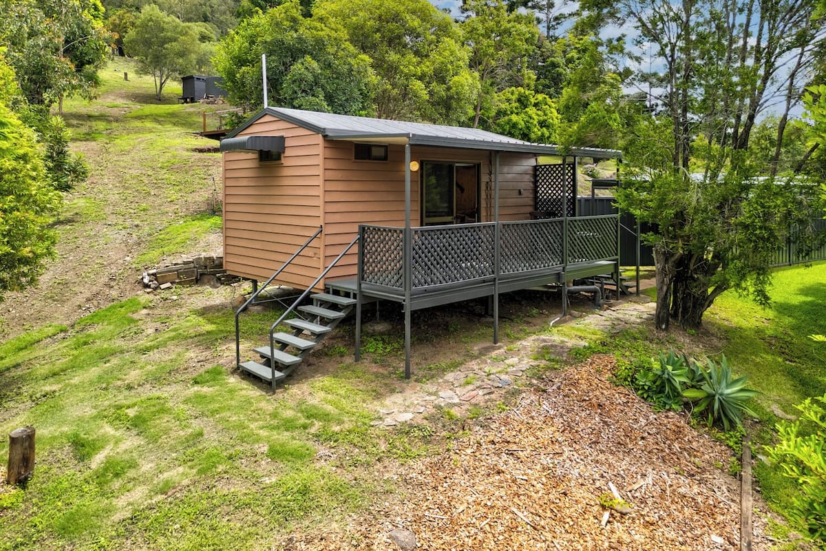 A small cabin with a porch, steps leading up to the entrance, and surrounded by lush greenery.
