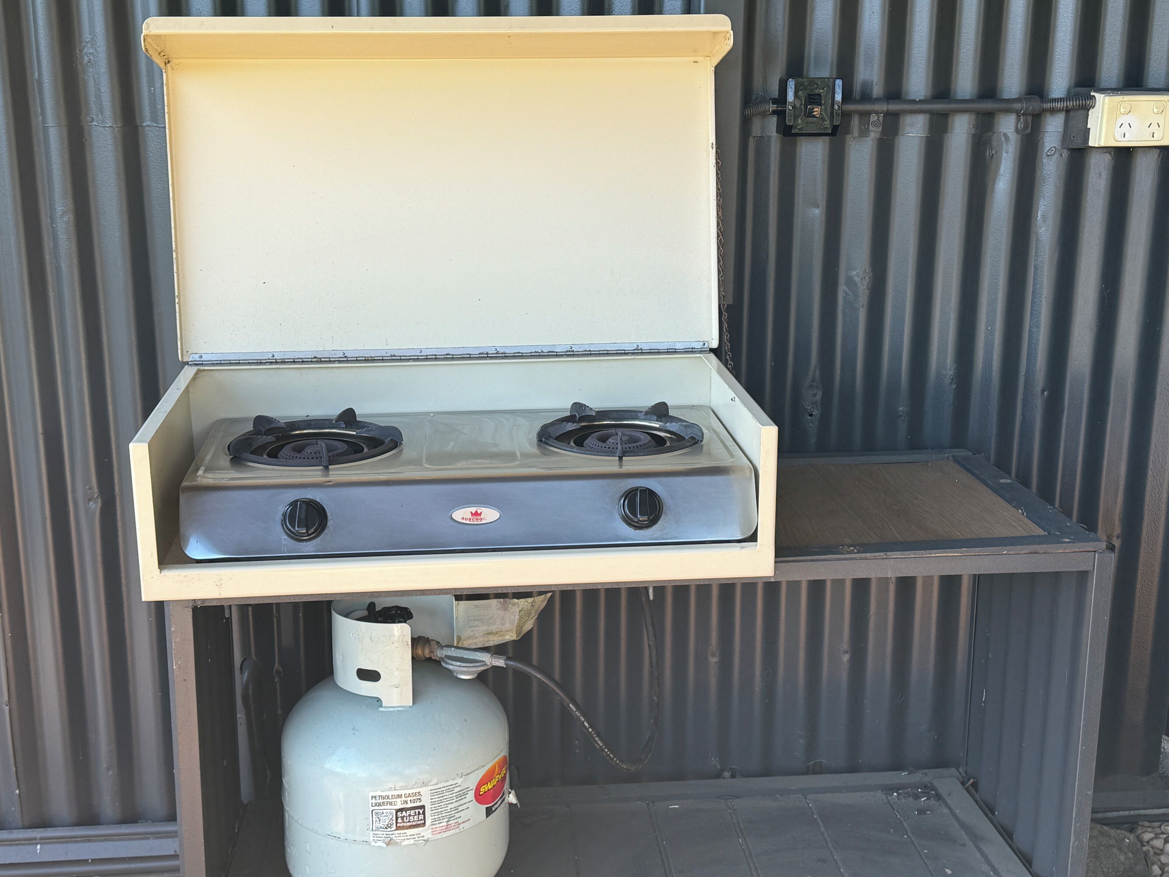 Een draagbaar gasfornuis met twee branders, een gasfles en een metalen behuizing.