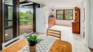 Una cocina moderna con refrigerador, pileta y gabinetes de madera. En primer plano, una mesa de comedor con sillas y una planta.