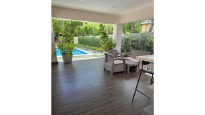 Amplia sala de estar con piso de madera, una mesa de comedor con sillas y vistas a una piscina y áreas verdes.