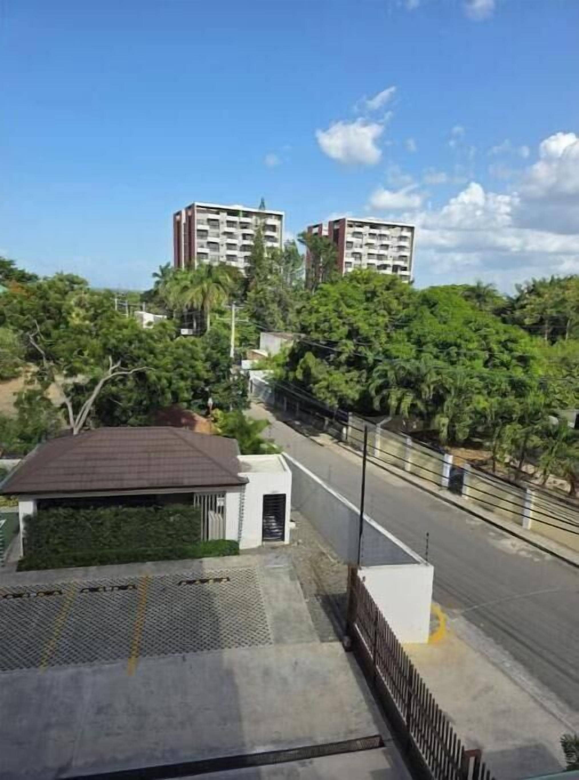 Zona residencial con dos edificios de gran altura, una calle pavimentada y un pequeño edificio blanco con techo marrón.