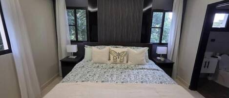 Une chambre à coucher avec un grand lit, deux tables de chevet avec des lampes, une fenêtre avec des rideaux et un appareil de climatisation.