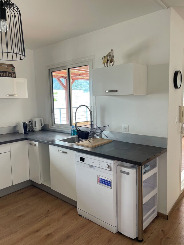 Una cocina moderna con armarios blancos, lavavajillas integrado, encimera de madera y ventana con vistas al exterior.