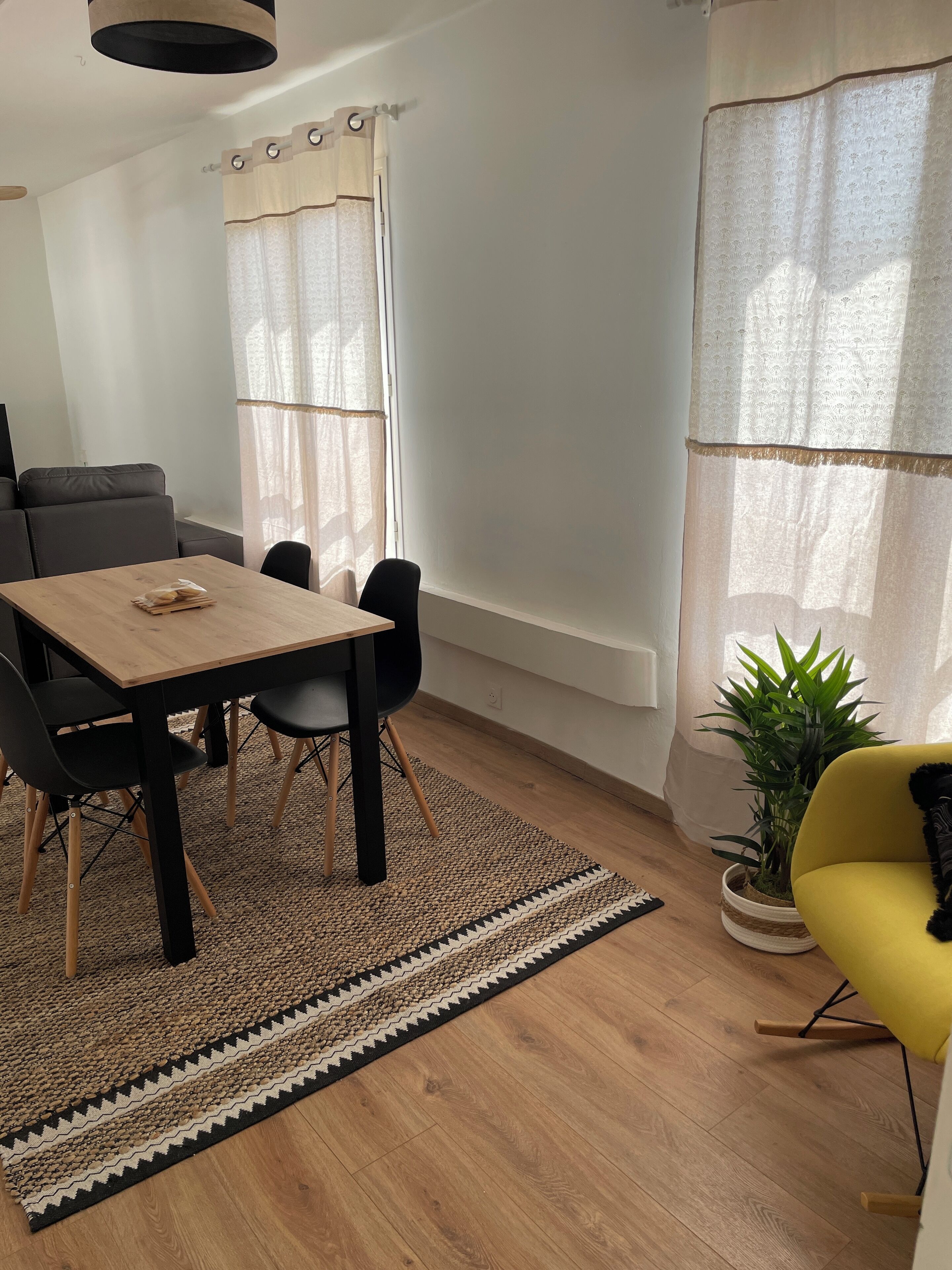 A modern dining area with a wooden table and black chairs, a grey sofa, and a yellow armchair.