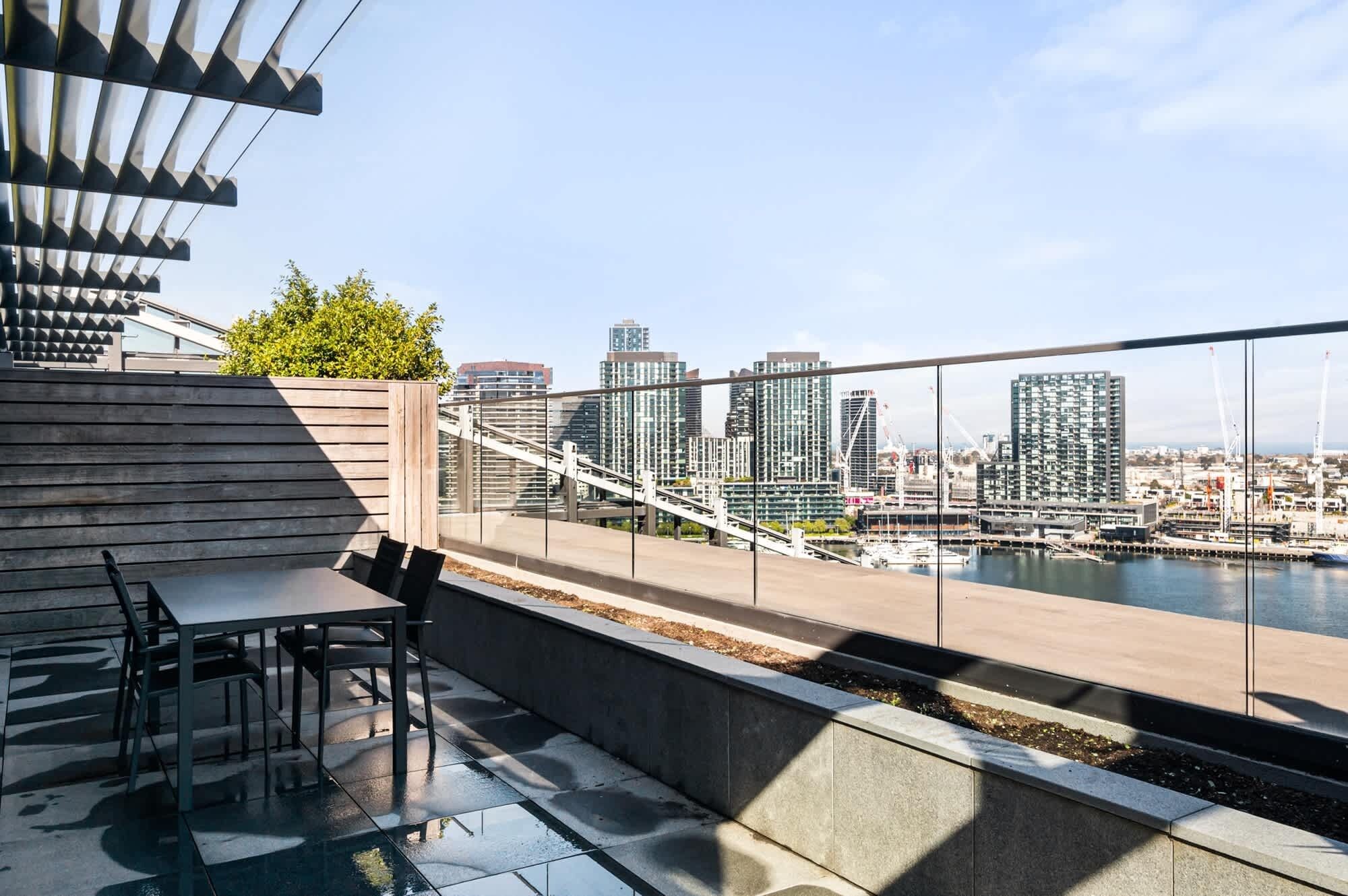 A rooftop terrace with a view of a city skyline, a table with chairs, and a railing.