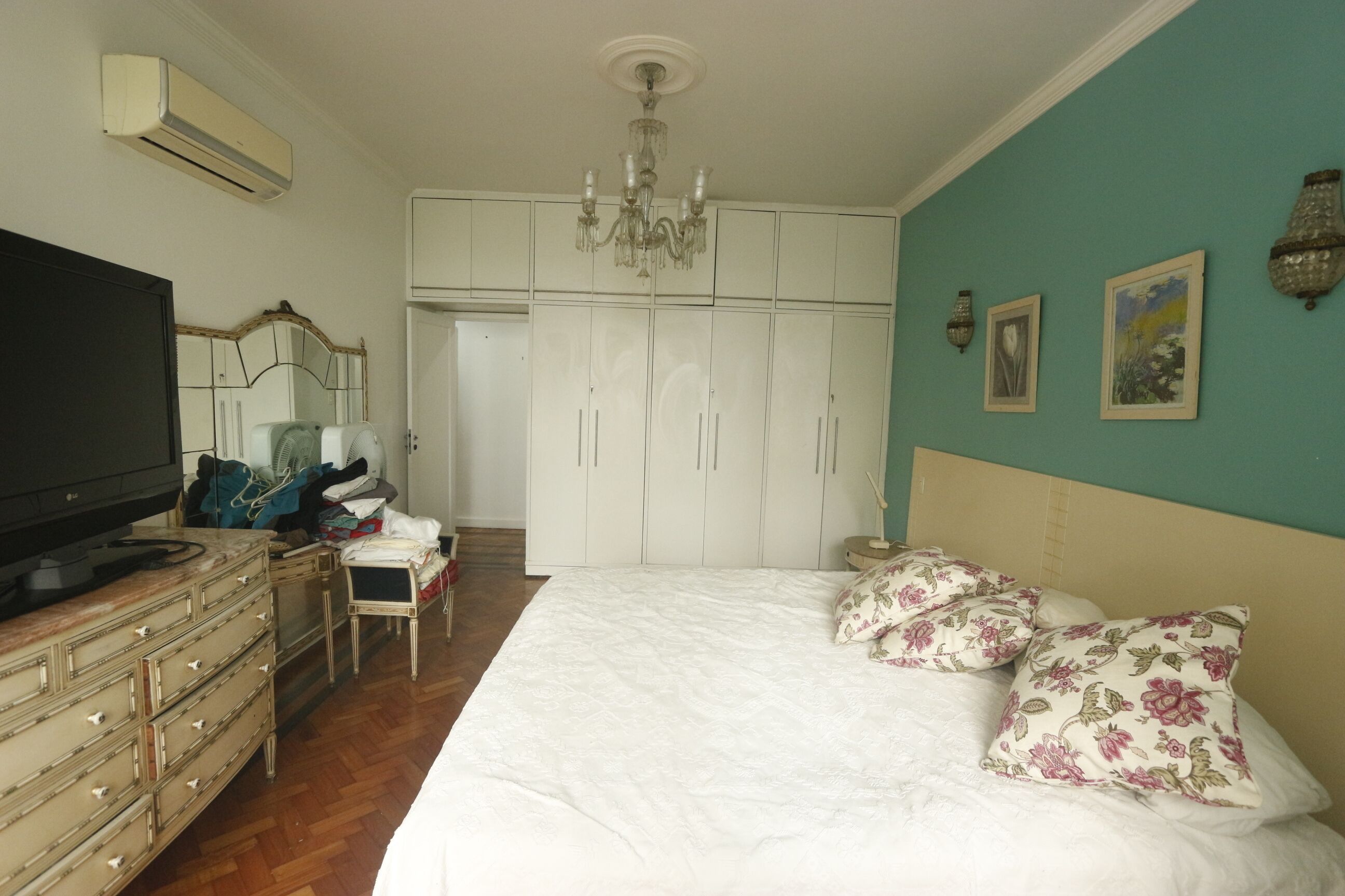 Une chambre à coucher avec un grand lit, une commode, un téléviseur, une armoire et un lustre.