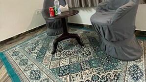 A room with a grey armchair, a small table with a bottle and a tissue box, and a patterned rug. - Amrai Valley Resort (Desuri)