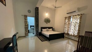 A bedroom with a bed, a desk, and a chair. There is a bathroom visible through an open door. - Amrai Valley Resort (Desuri)