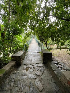 A stone bridge with metal railings, surrounded by lush green foliage. - Amrai Valley Resort (Desuri)