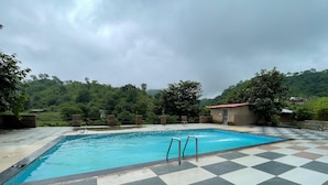 A swimming pool with checkered tiles and metal ladders, surrounded by greenery and hills. - Amrai Valley Resort (Desuri)