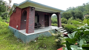 A small, single-story brick building with a covered porch and a few chairs. - Amrai Valley Resort (Desuri)