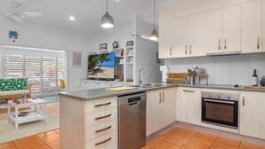 Cuina moderna amb rentavaixelles, forn i zona de menjador amb sofà i taula.