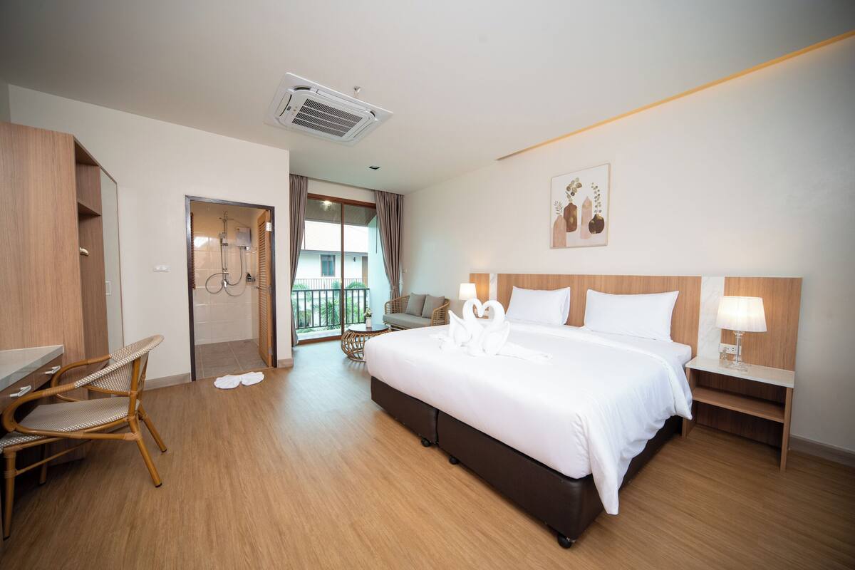 A hotel room with a large bed, a wooden wardrobe, a seating area with a chair and table, and a balcony with a view.
