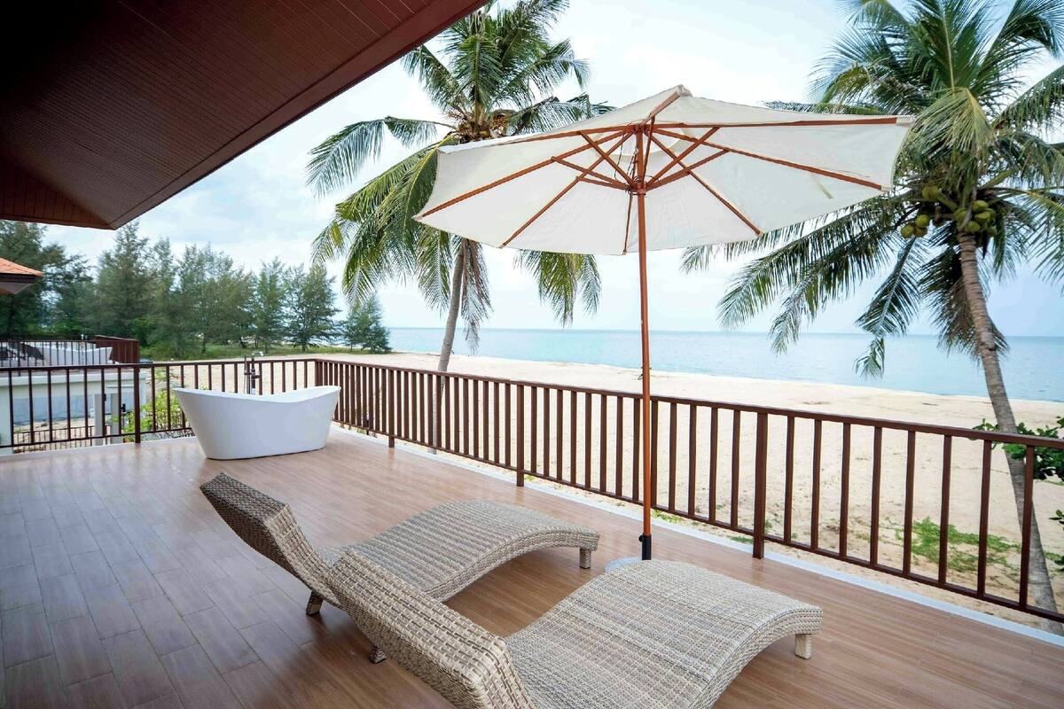 A balcony with wicker lounge chairs, a white bathtub, and a large umbrella.