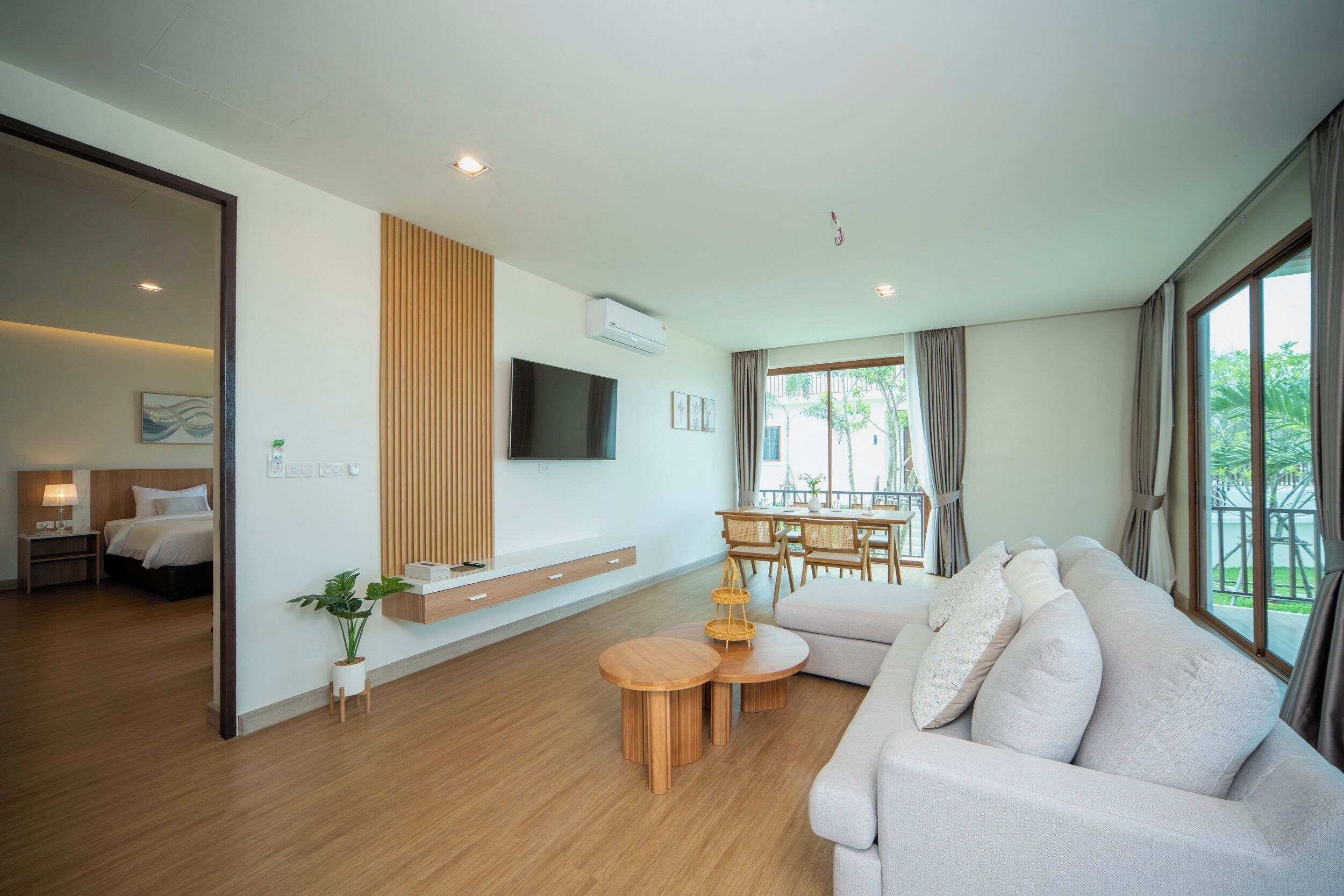 A modern living room with a sofa, a dining table, and a TV mounted on the wall.