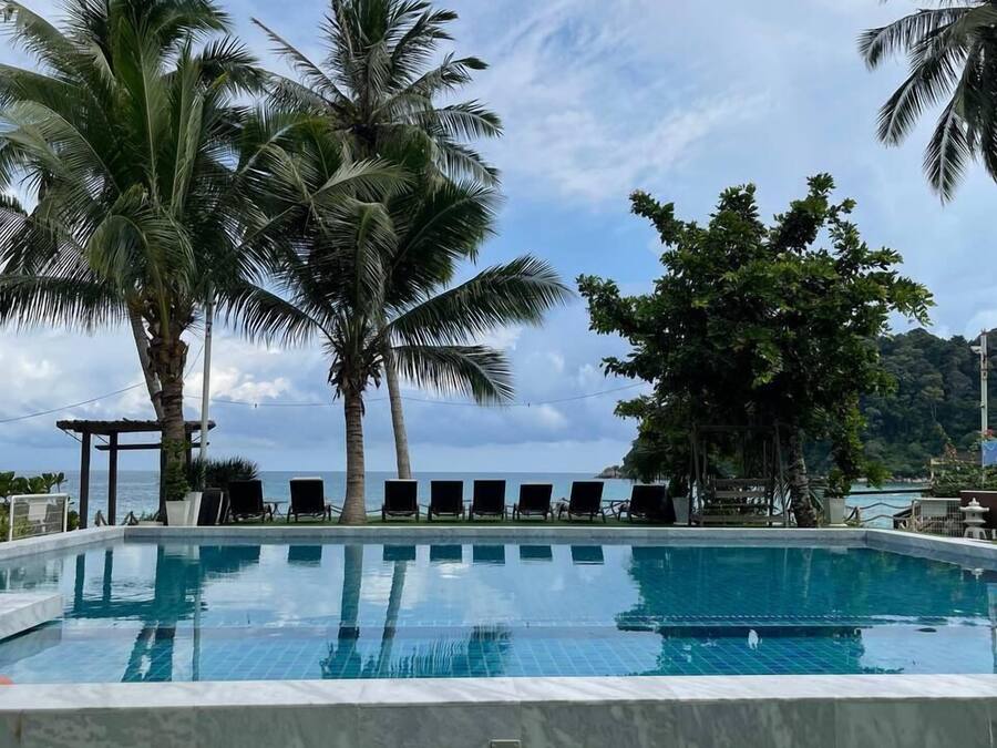 A pool with lounge chairs, palm trees, and a view of the ocean.