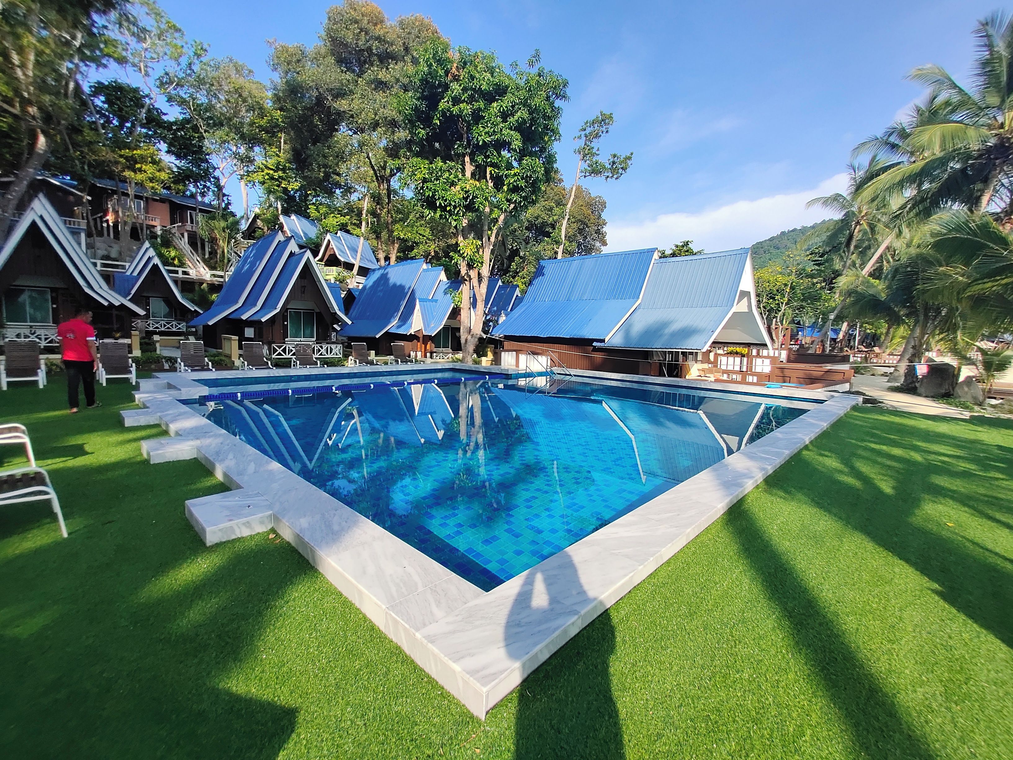 A swimming pool with a clear blue water, surrounded by grass and trees.