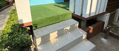 A concrete staircase leading to a porch with a blue wall and a small garden area.