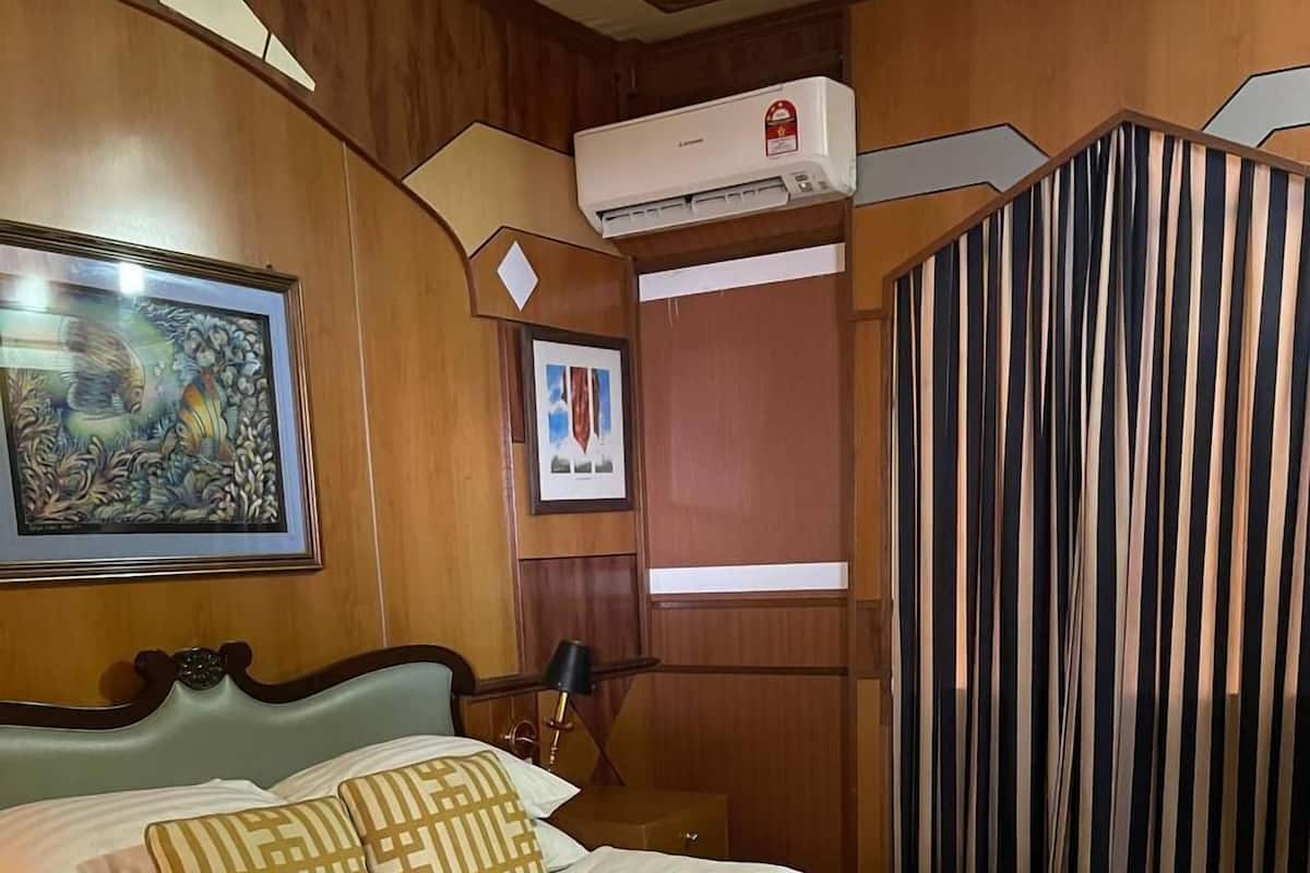 A hotel room with a bed, a nightstand, a lamp, an air conditioning unit, a framed picture, and a striped curtain.