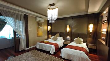 A hotel room with two beds, a large rug, a chandelier, and a view of the outdoors.
