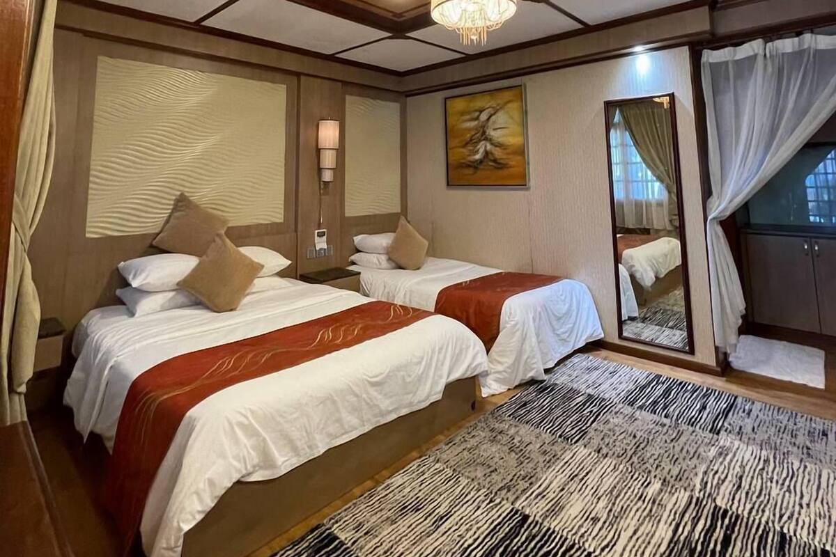 A hotel room with two beds, a chandelier, a large mirror, and a view of the outside.
