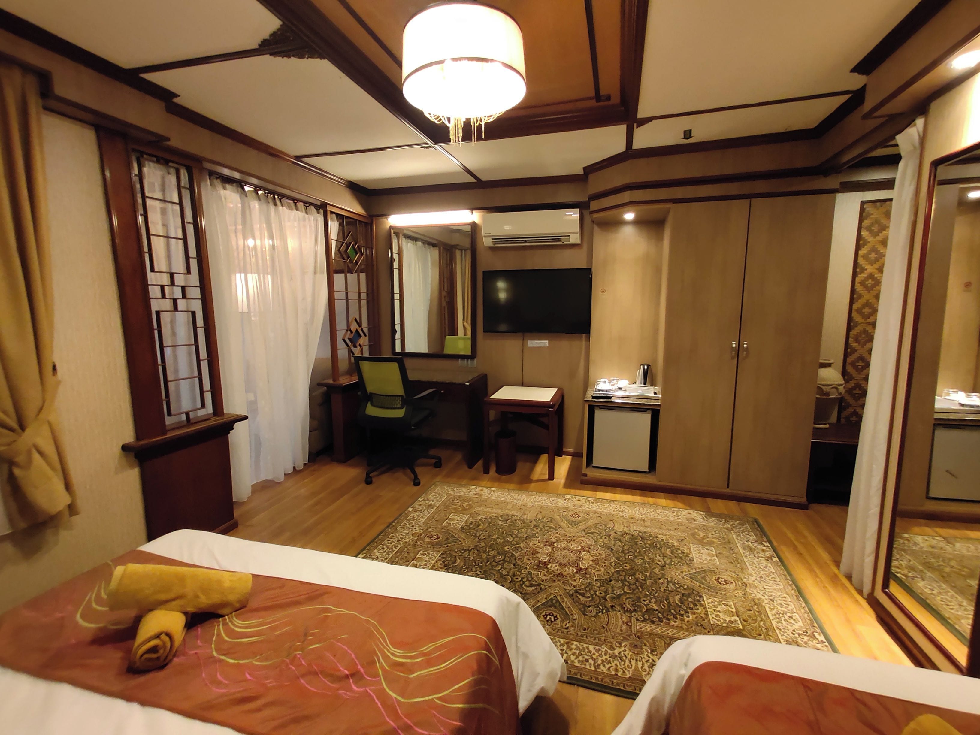 Habitación de hotel con dos camas, un escritorio, una silla, un televisor, un armario y un refrigerador pequeño.
