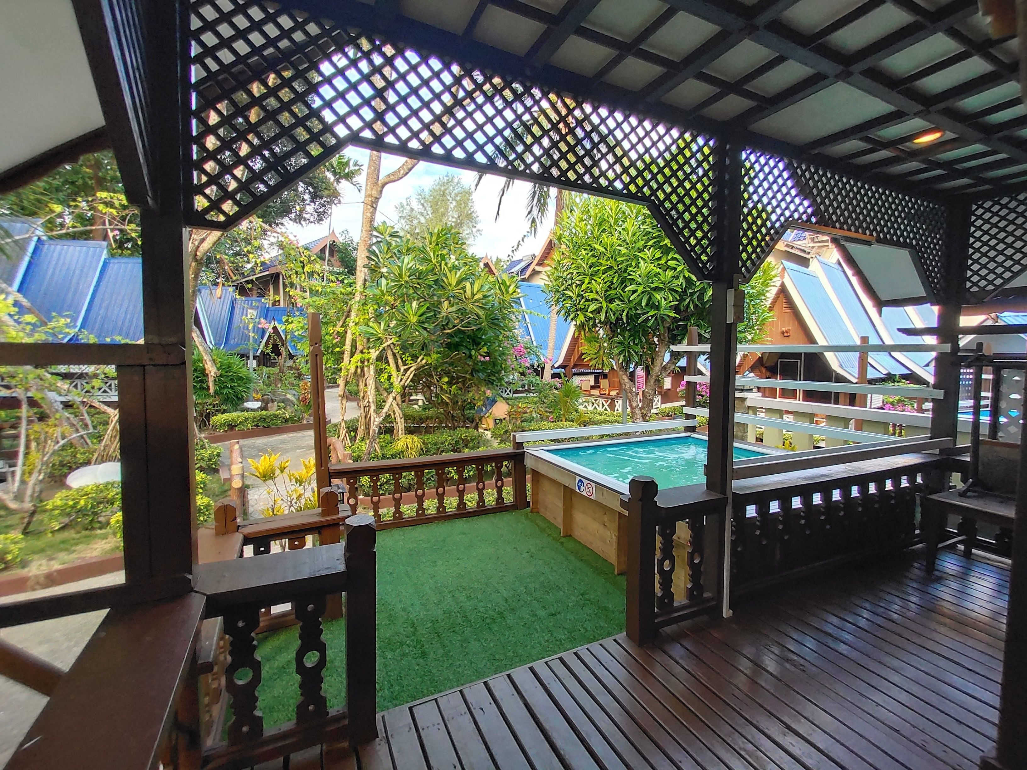 Un espacio exterior cubierto con piscina, terraza de madera y vista a una zona residencial con casas y vegetación.