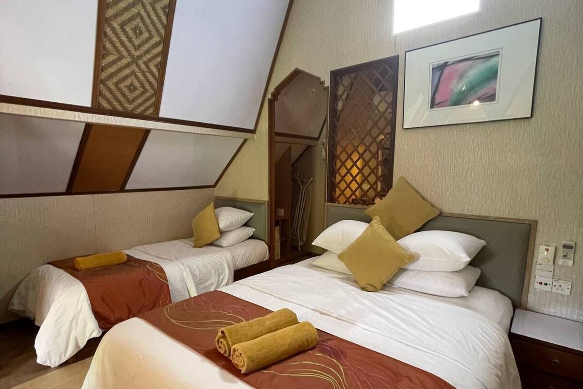 A room with two beds, each with a brown and white bedspread and pillows. There are two wall-mounted light fixtures and a framed picture on the wall.