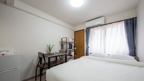 Une chambre à coucher comprenant un lit, un bureau avec une chaise, une petite table, une plante en pot et une armoire.
