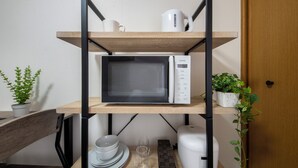 Une cuisine avec un four à micro-ondes posé sur une étagère, une machine à café et une plante en pot.