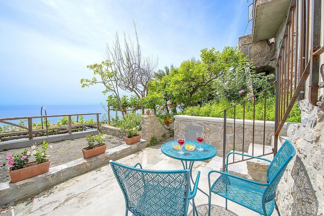Une terrasse avec une table et des chaises, des plantes en pot et une vue sur la mer.