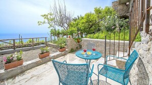 Una terraza con mesa y sillas, plantas en macetas y vistas al mar.