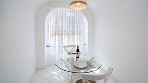 Un comedor con una mesa de vidrio, sillas blancas y una botella de vino.