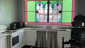 A kitchen with white cabinets, a stove, a sink, and a window with colorful stained glass. - Lovely 4-bedroom villa, save on kennel fees and bring your dog! (Waihi)