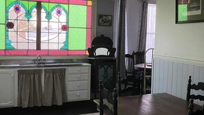 A dining area with a wooden table and chairs, a patterned rug, a kitchen with a sink and cabinets, and a stained glass window. - Lovely 4-bedroom villa, save on kennel fees and bring your dog! (Waihi)