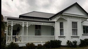 A white two-story house with a porch, a covered front porch area, and a small garden in front. - Lovely 4-bedroom villa, save on kennel fees and bring your dog! (Waihi)