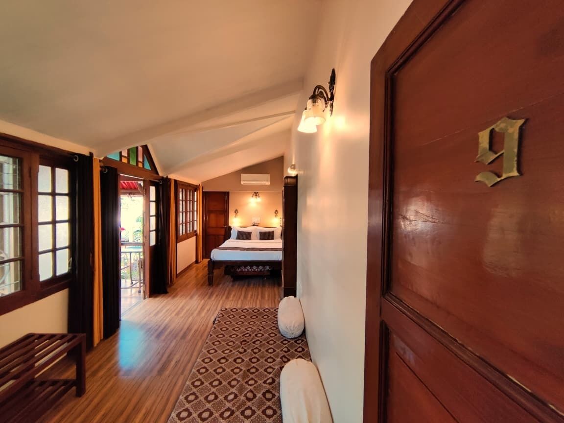 Un pasillo con un banco de madera, un tapete estampado, una cama con almohadas y una puerta con un número.