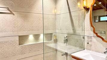 A modern bathroom with patterned tiles, a glass shower enclosure, a wooden-framed mirror, and a white sink.