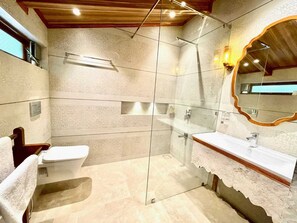 Un baño con ducha envuelta en vidrio, tocador de madera y un espejo grande.
