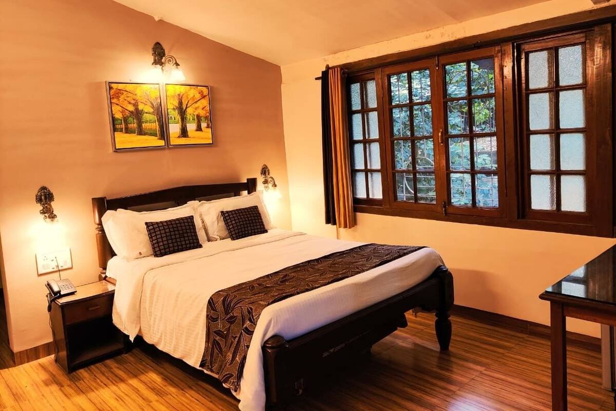 Un dormitorio con cama de madera, dos lámparas de noche, una mesita de noche, una ventana con cortinas y un cuadro en la pared.