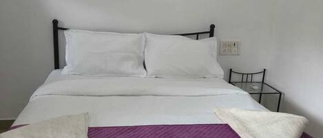 A neatly made bed with white linens, a purple blanket, and a decorative pillow.