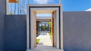 A modern entrance with a glass door leading to a covered outdoor area. - Villa Linaria Pecatu (Ungasan)